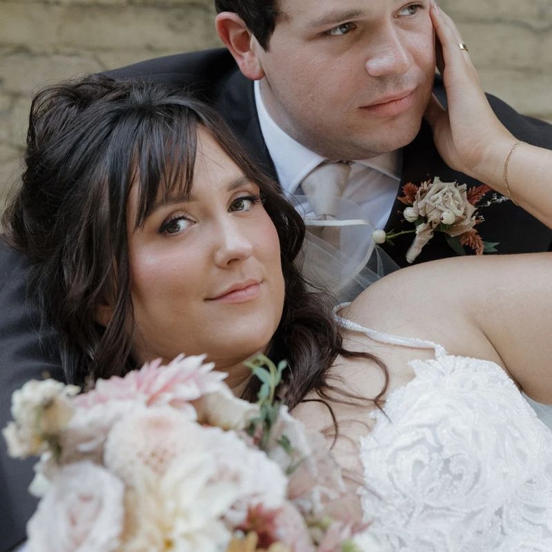 Bride resting against her groom with a blush and cream bouquet and a dried-flower boutonniere at The Fitzgerald in Milwaukee